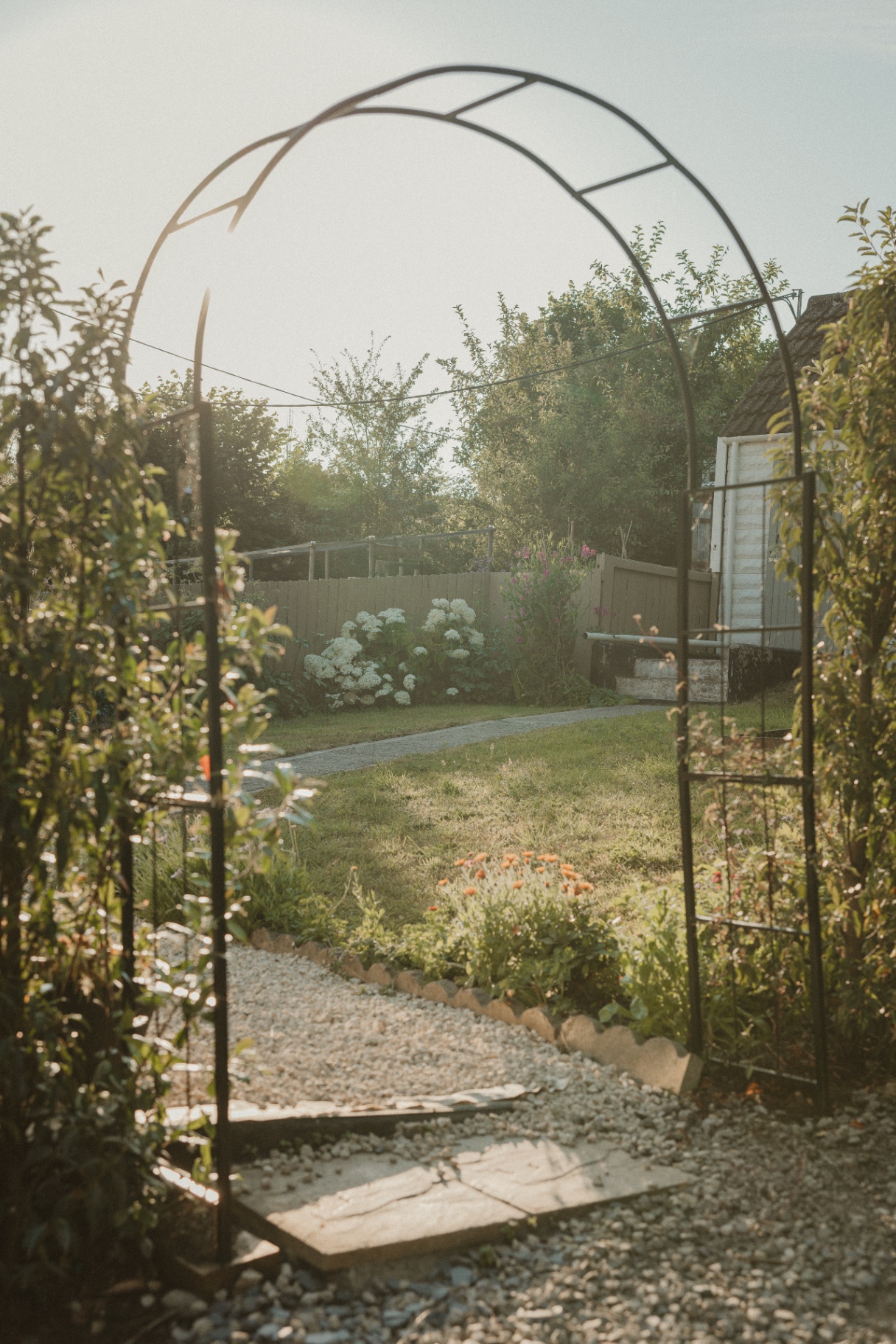The Guesthouse - garden arch framing the flower beds and lawn at golden hour