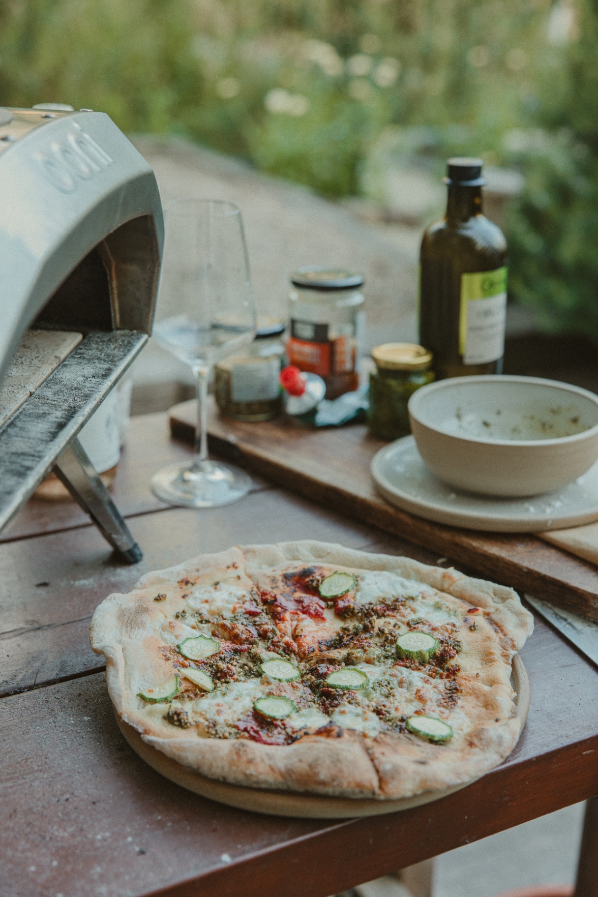 Freshly cooked Ooni pizza on a wooden table with olive oil and toppings