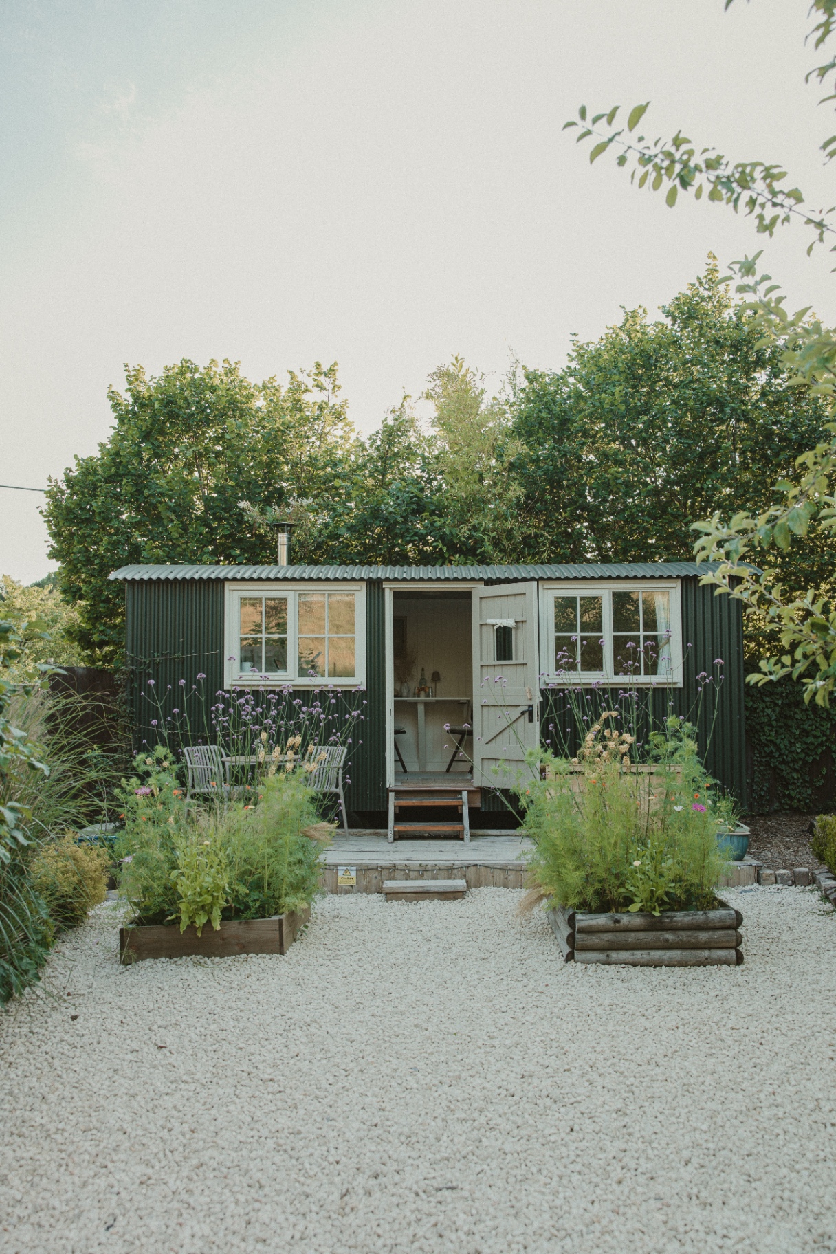 Fern - front view of the green shepherd's hut framed by verbena and cottage garden planting