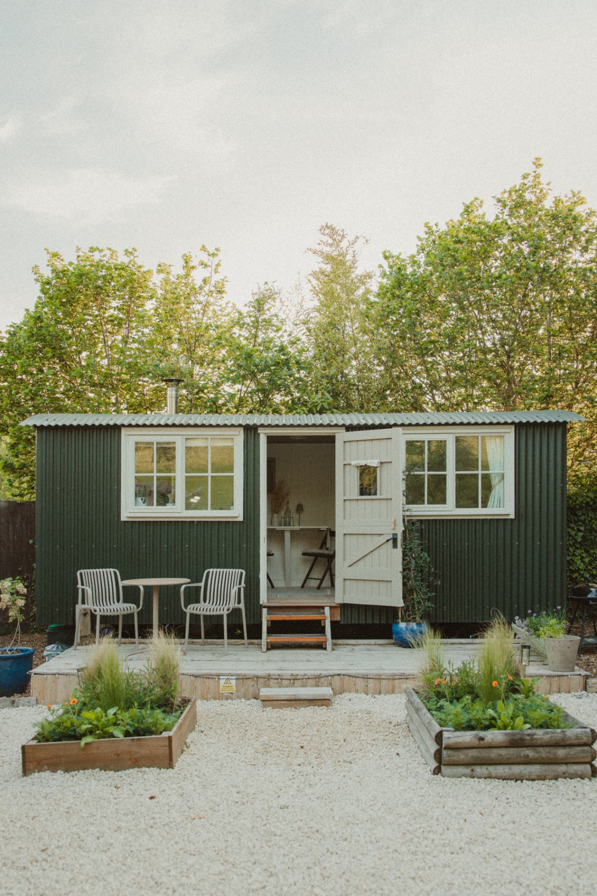 Fern - front view of the green shepherd's hut with open door, chairs and raised vegetable beds