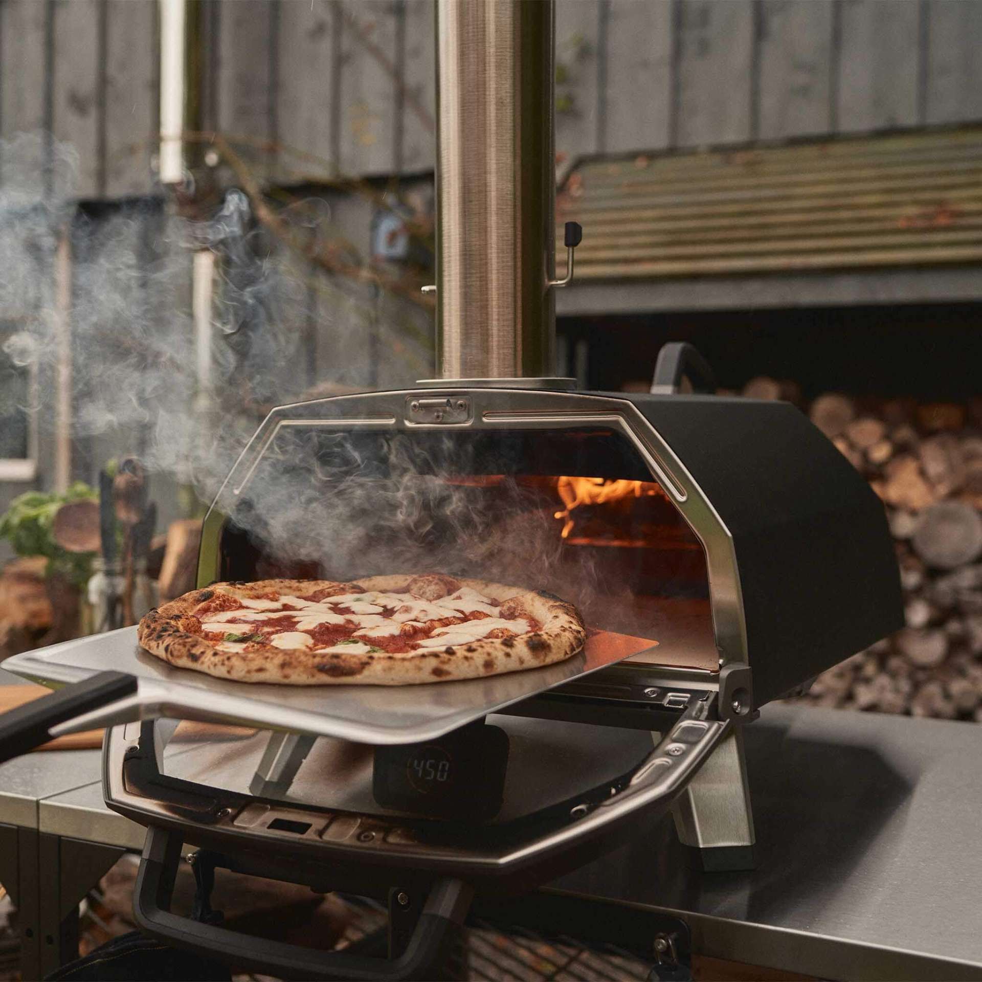 Wood-fired Ooni pizza oven cooking a freshly made pizza outdoors