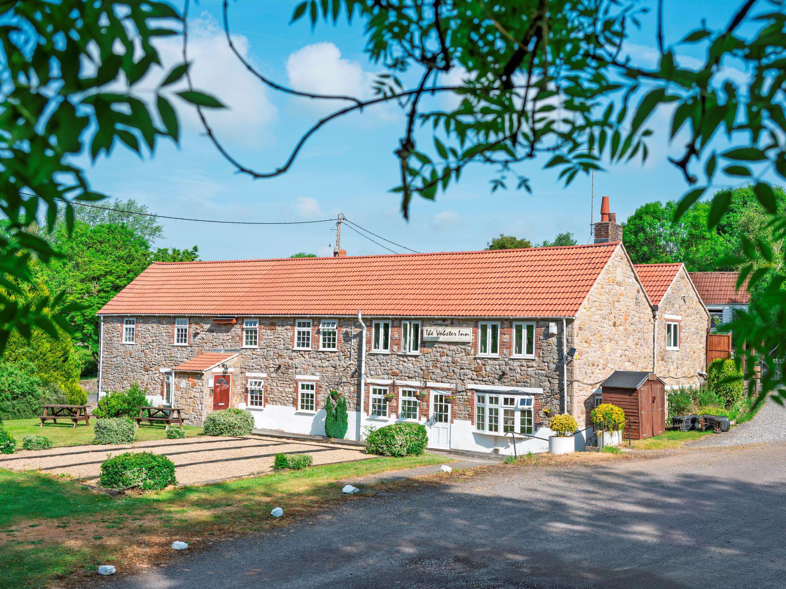 The Vobster Inn - a stone Somerset farmhouse framed by willow branches under a blue summer sky